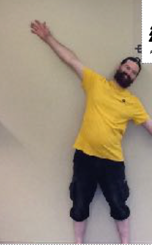 A man with a beard is standing in front of a wall with his arms outstretched.