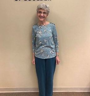 A woman is standing in front of a wall wearing a blue shirt and blue pants.