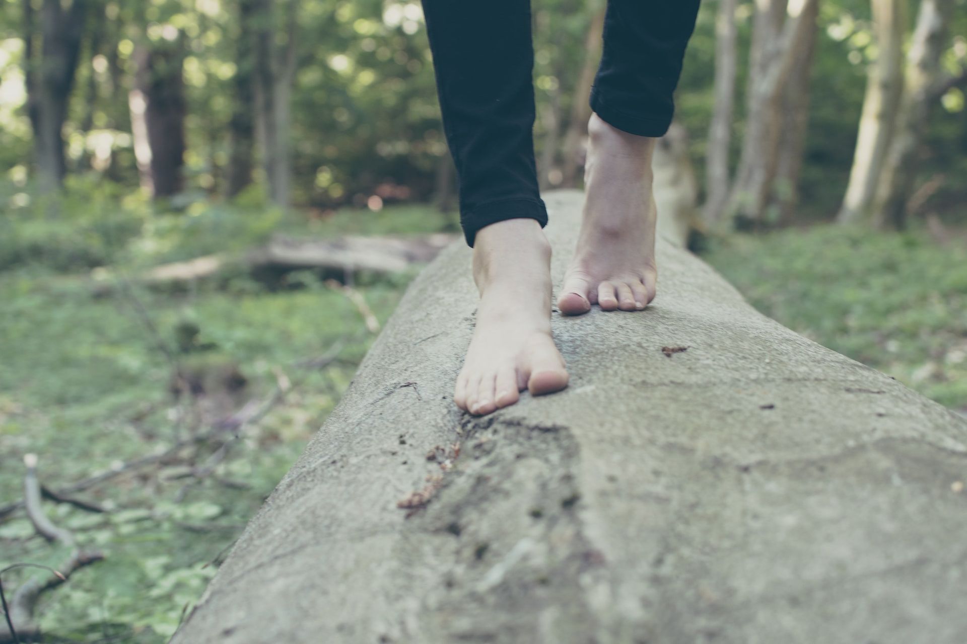 A person is walking barefoot on a log in the woods.