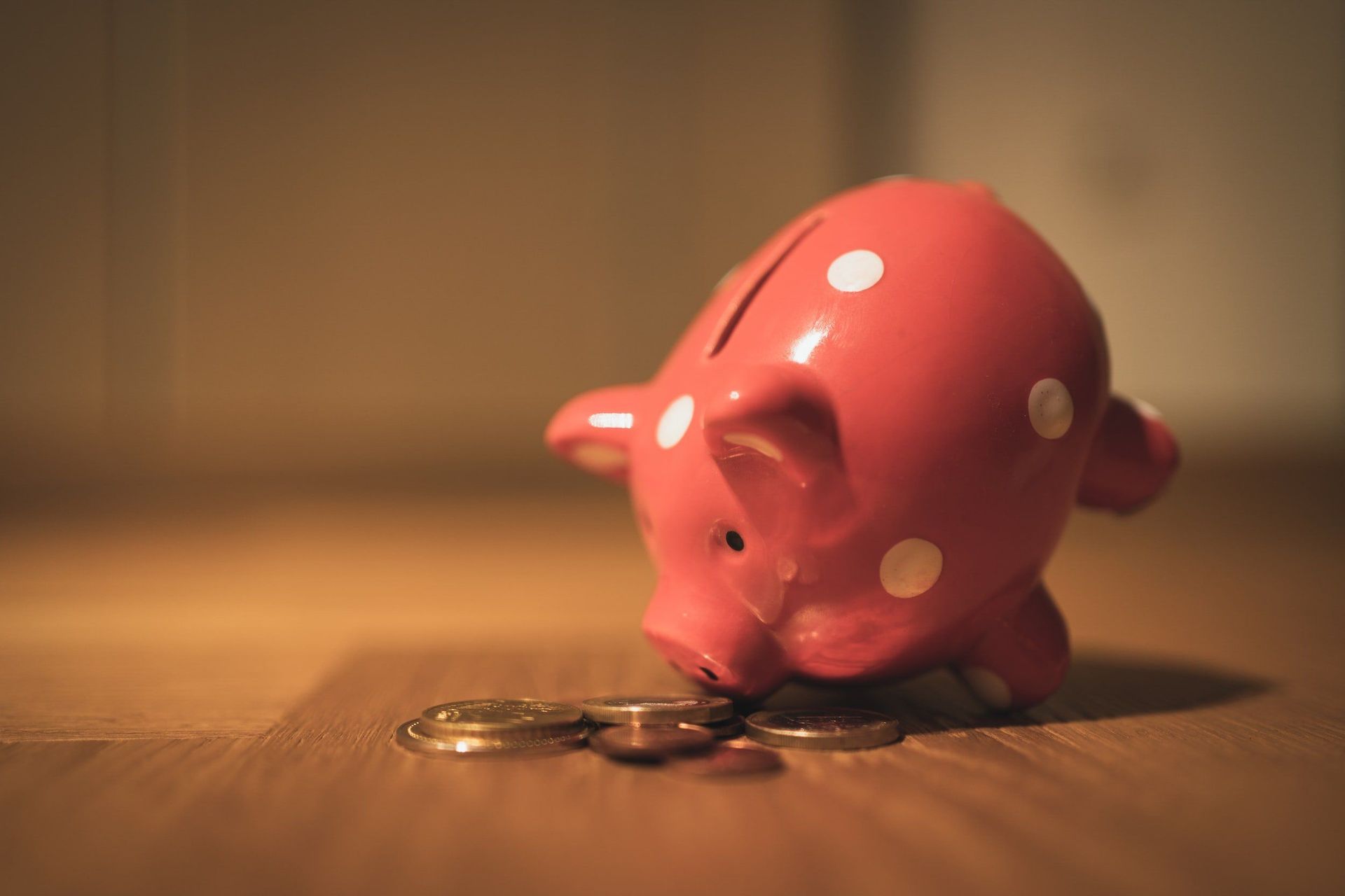 A red piggy bank is sitting on a wooden table next to a pile of coins.