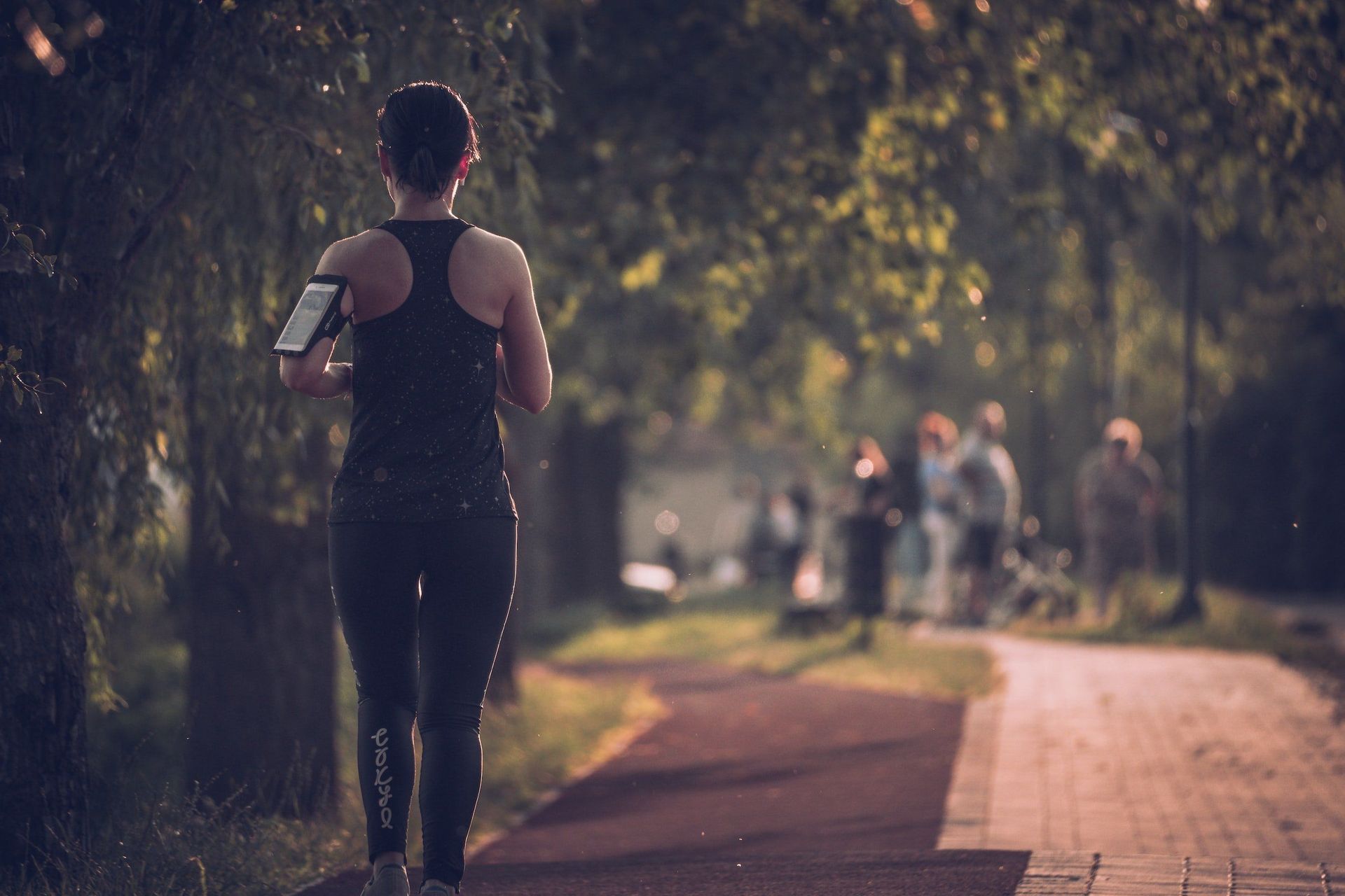 A woman is running down a path in a park while holding a cell phone.