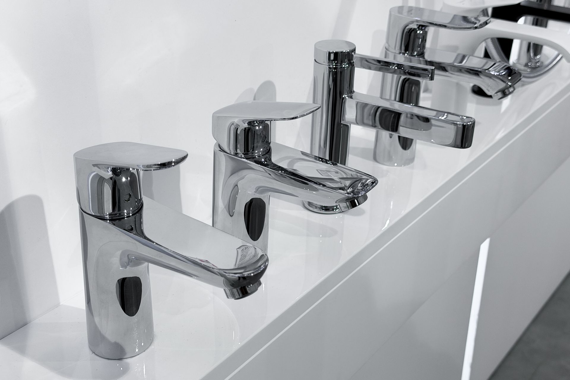 Row of chrome bathroom faucets on a glossy white sink counter