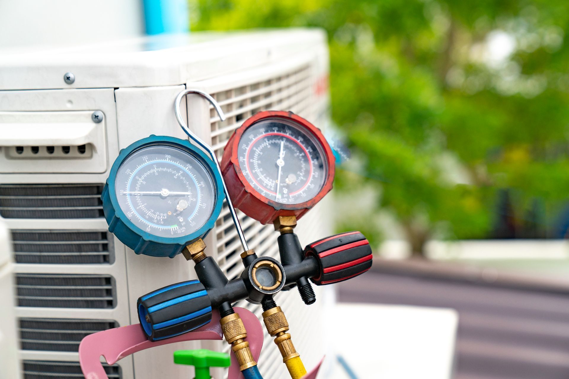 Colorful HVAC gauges connected to an outdoor air conditioner unit on a blurred green background