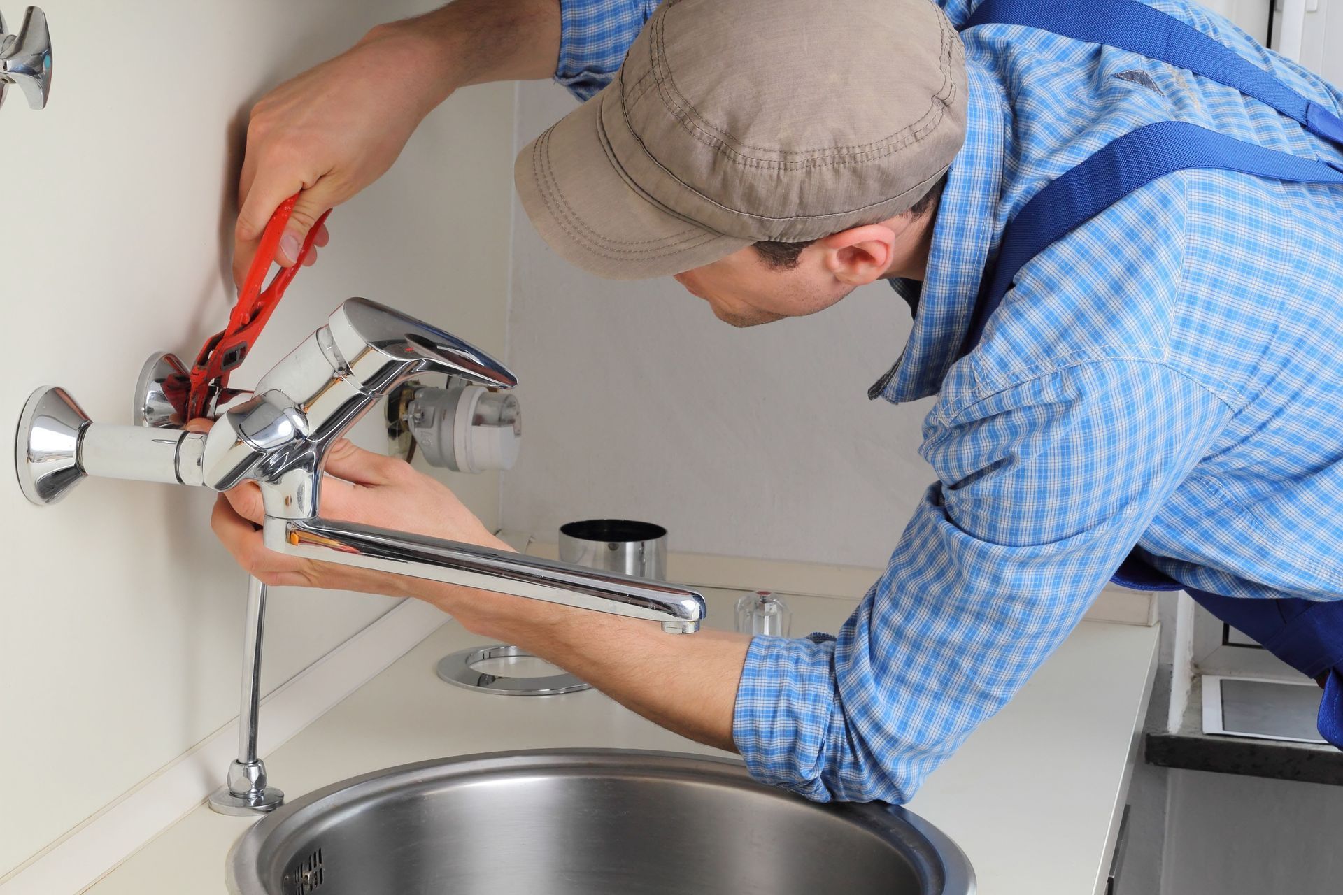 Person adjusting a chrome sink faucet with red pliers in a kitchen or bathroom sink area