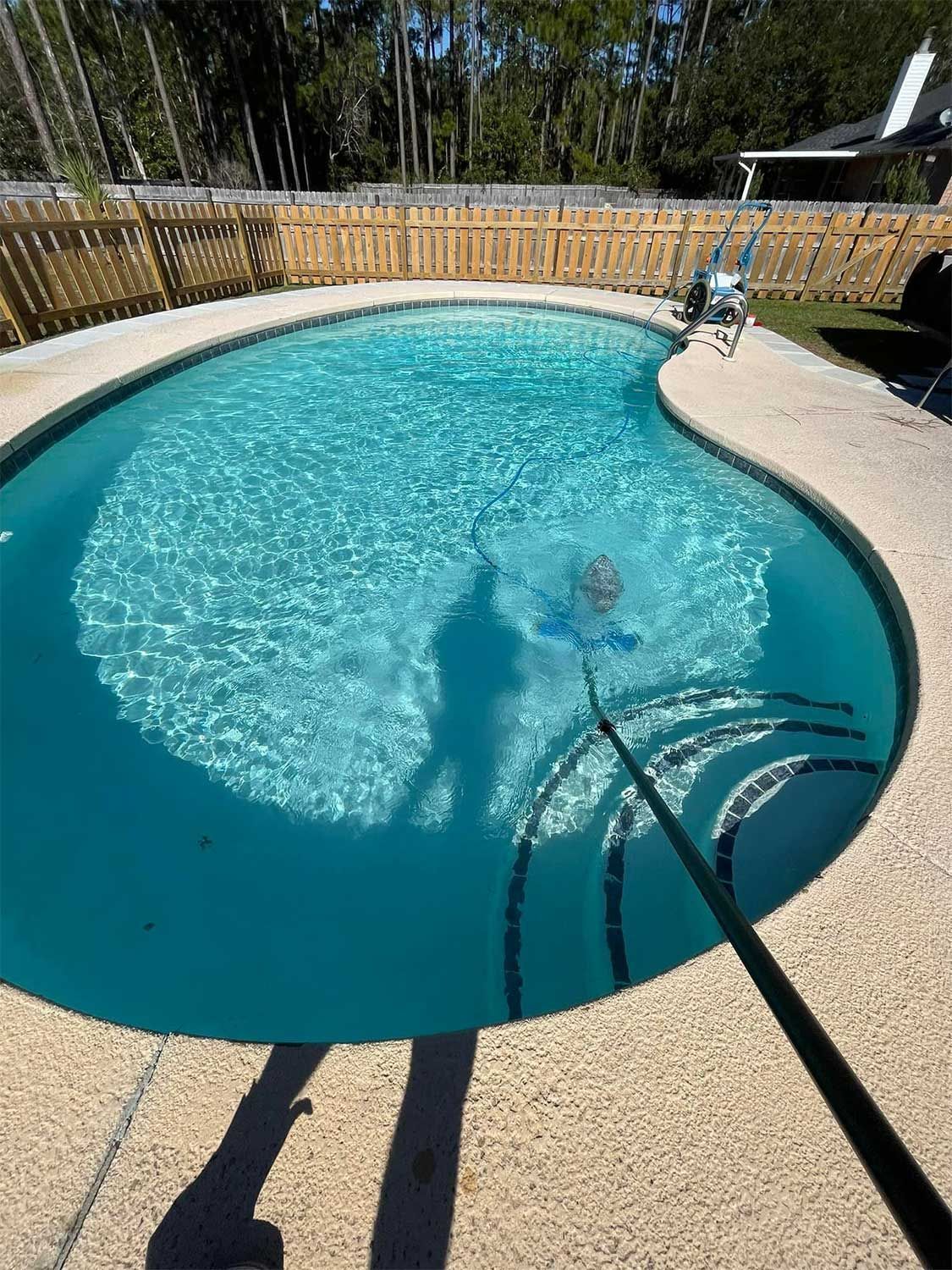 Worker Cleaning a Pool in Fenced Backyard