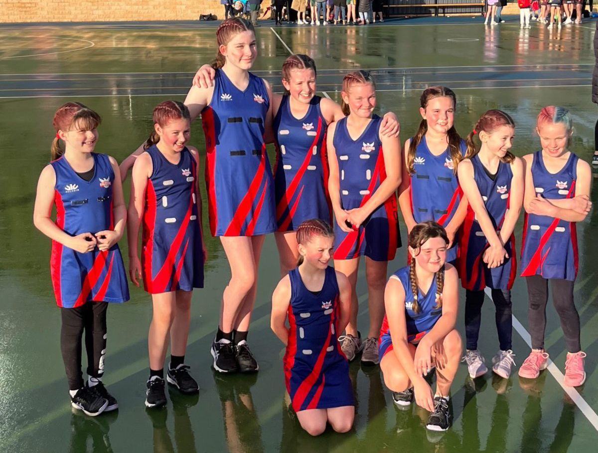 Youth netball team in blue and red uniforms posing on a netball court