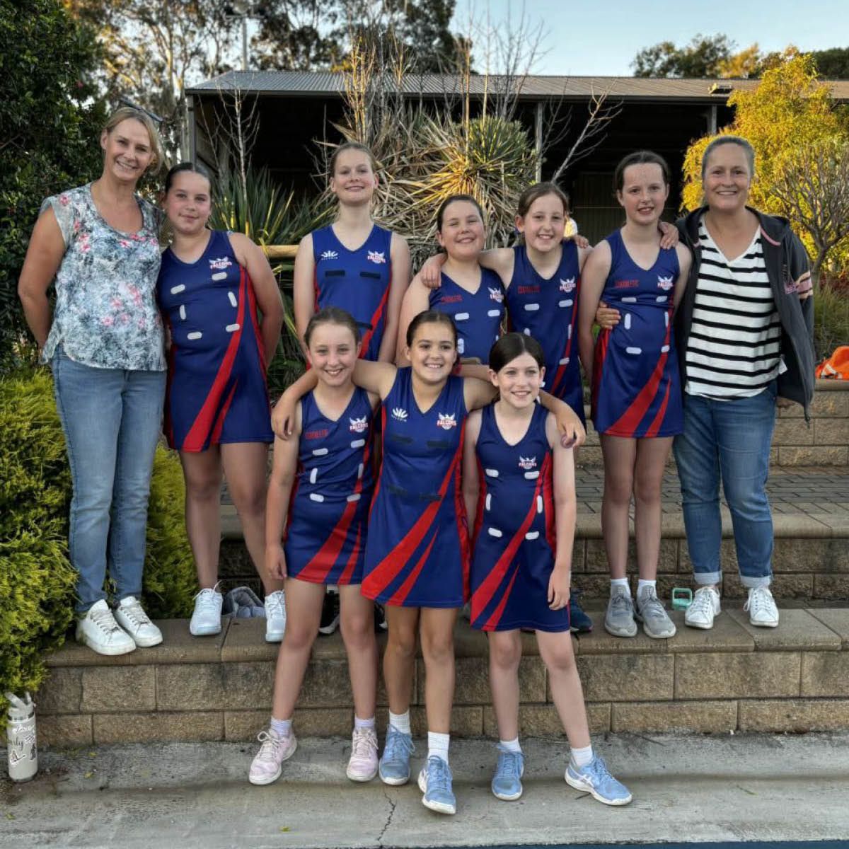 Group of seven women and girls in matching blue-and-red sports uniforms posing on outdoor steps
