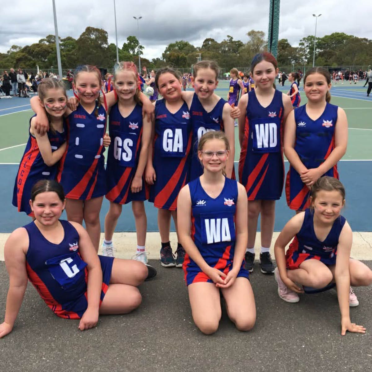 Netball team posing outdoors in blue and red uniforms on a court