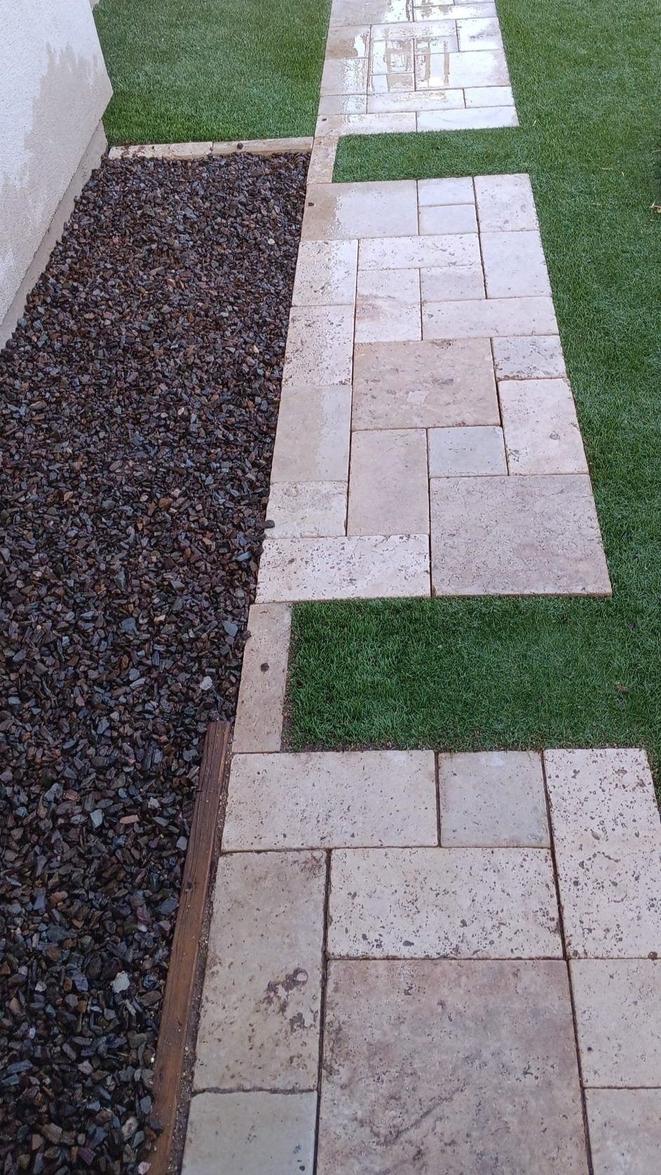 A stone walkway leading to a grassy area next to a gravel area.