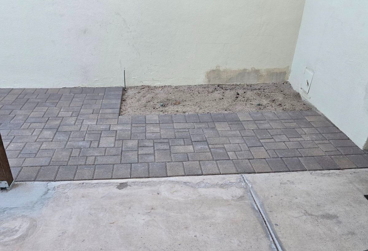A brick walkway is being built in front of a white wall.