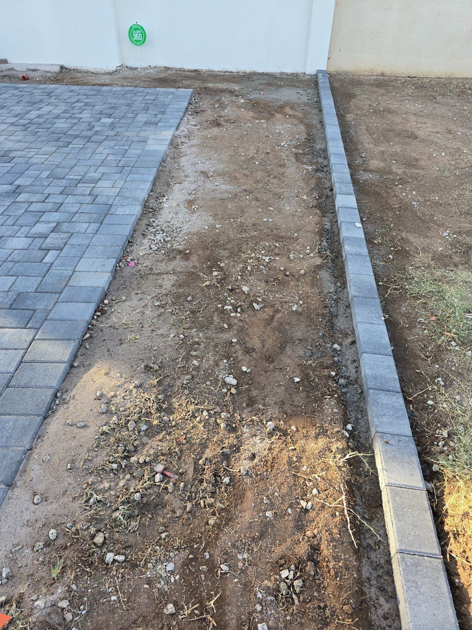 A brick walkway is being built next to a dirt field.