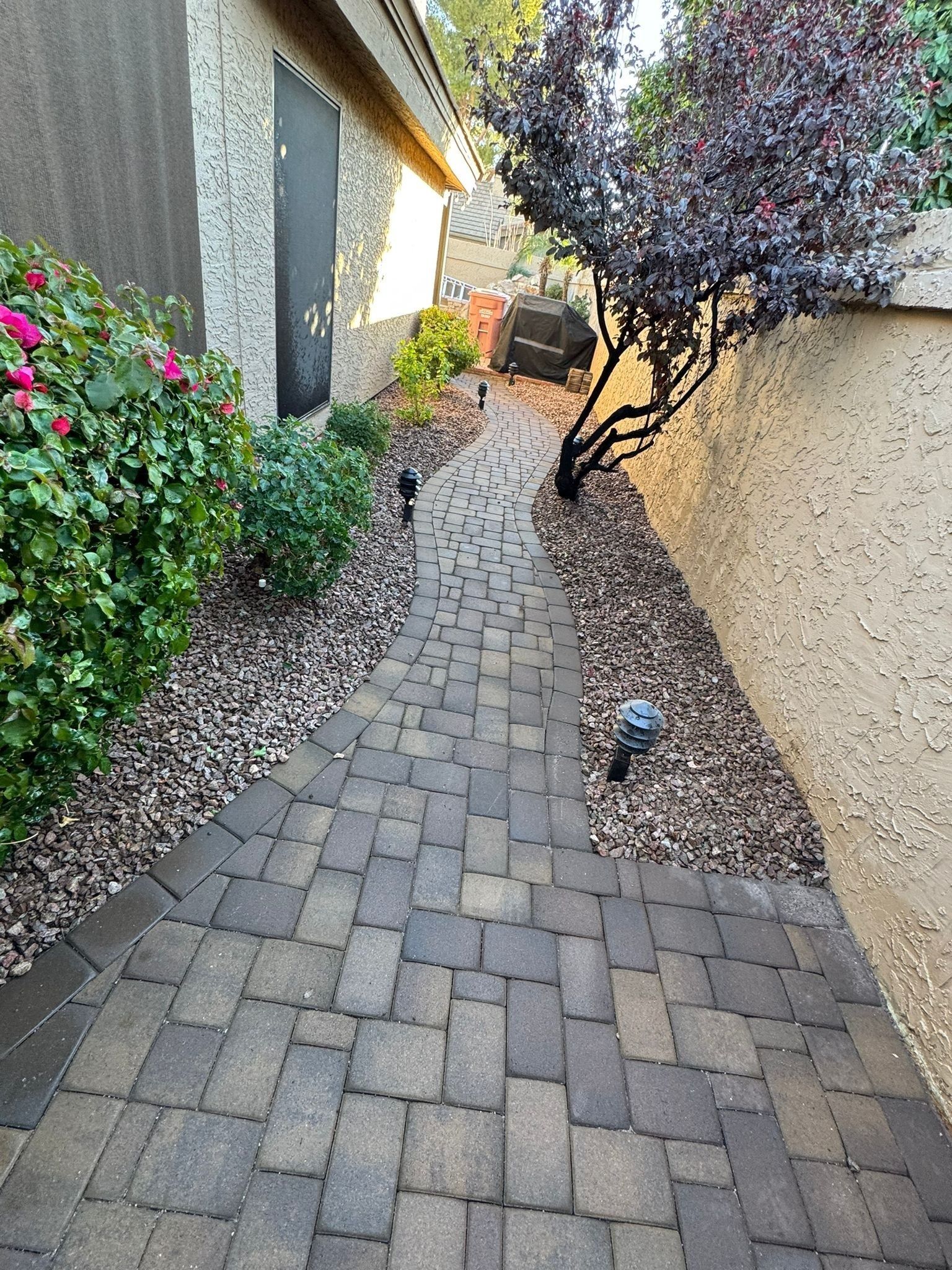 A brick walkway leading to a house with flowers on the side of it.