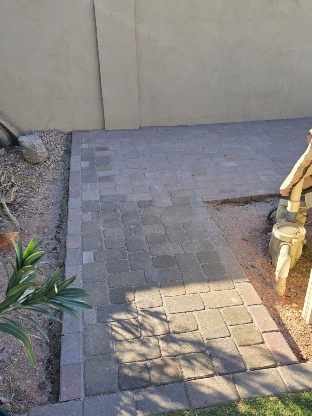 A brick walkway leading to a stone statue in a backyard.
