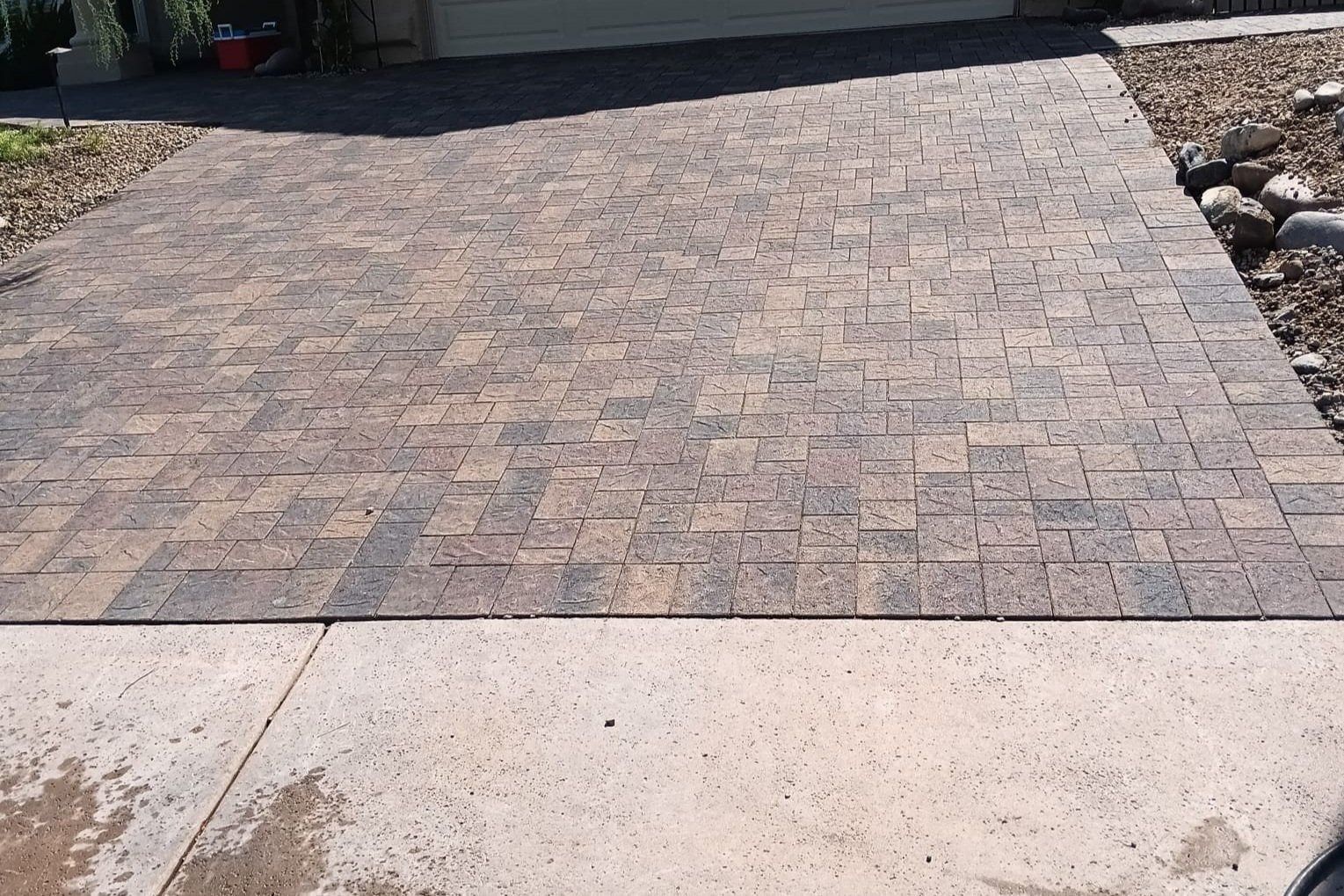 A brick driveway with a concrete sidewalk in front of a house
