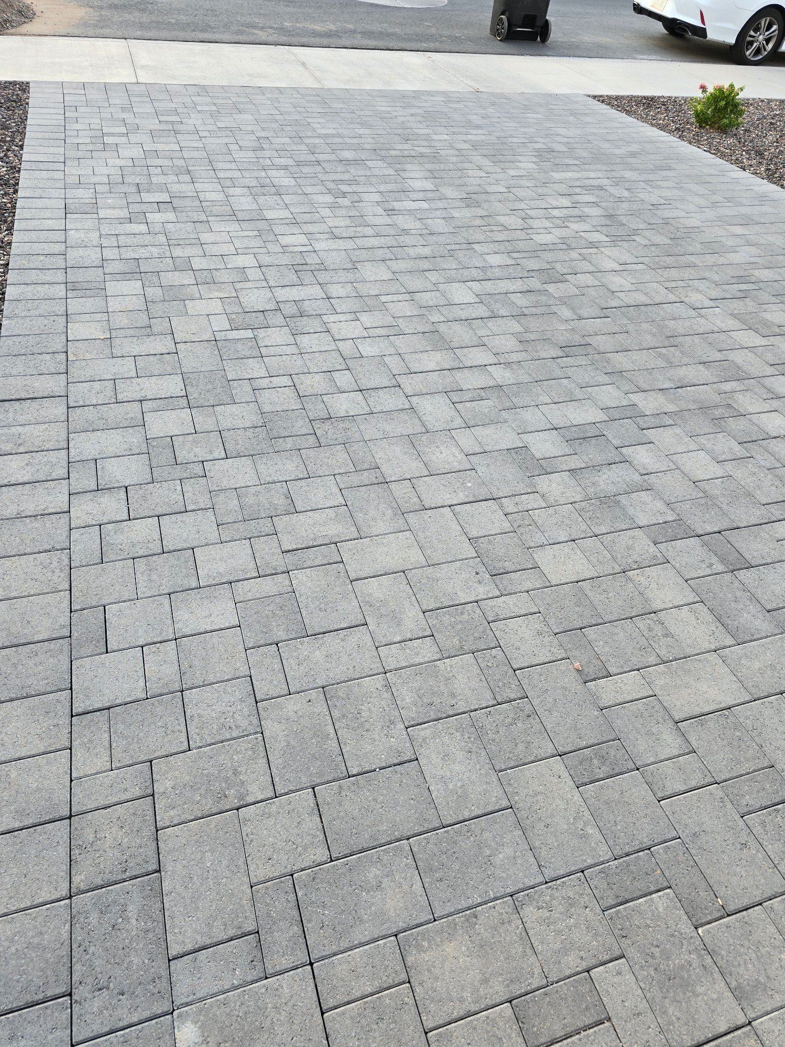 A brick driveway with a car parked in the background.