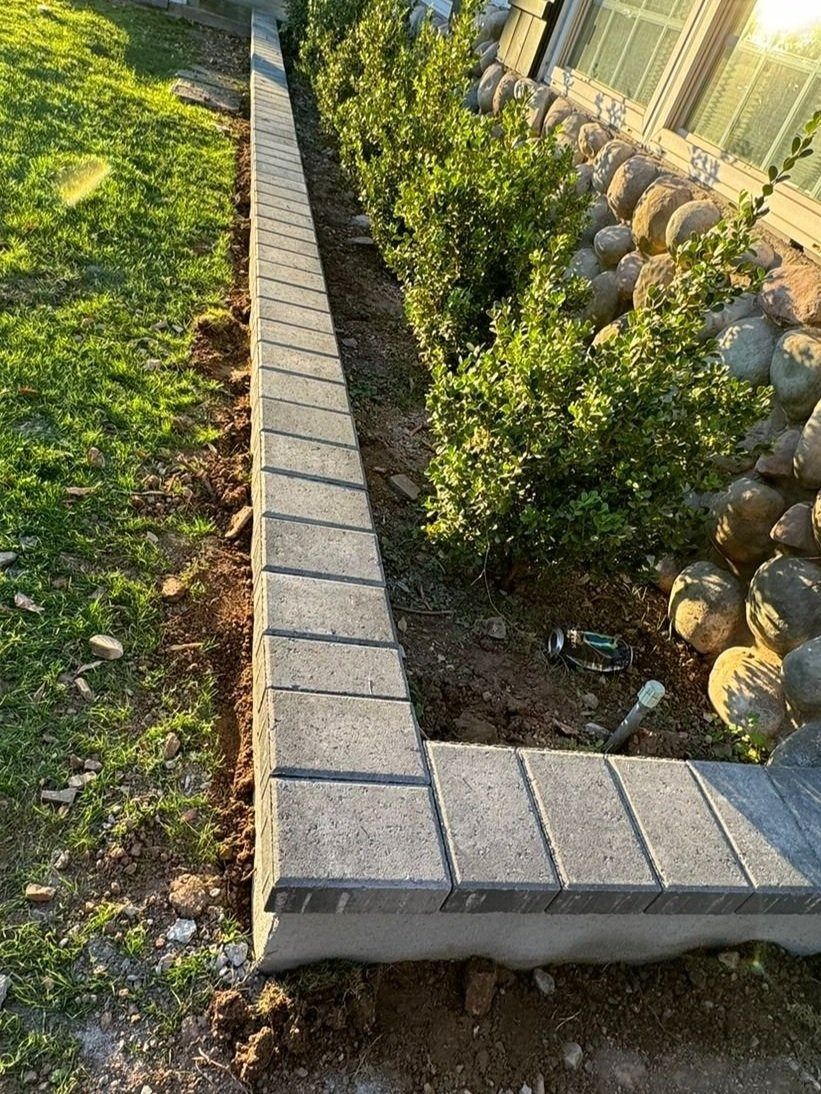 A brick wall is being built next to a bush in a garden.