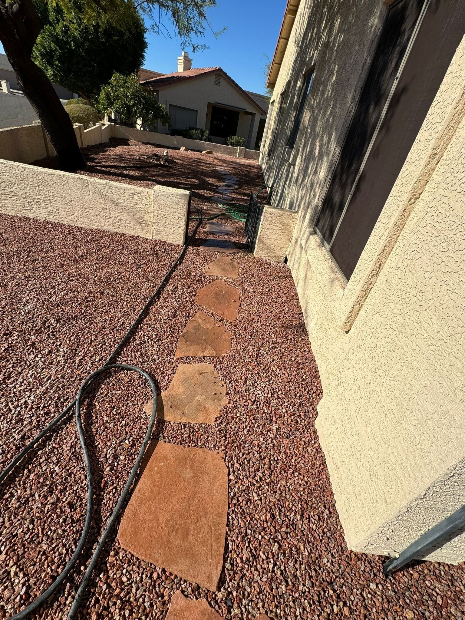 A hose is laying on the ground next to a walkway leading to a house.
