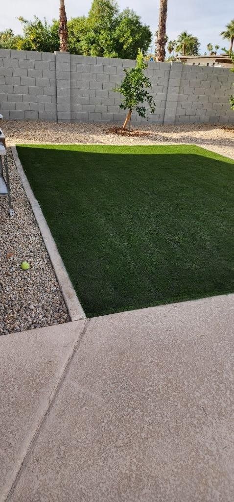 A backyard with a concrete fence and a lush green lawn.