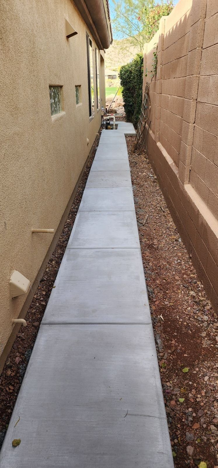 A concrete walkway leading to a house next to a brick wall.