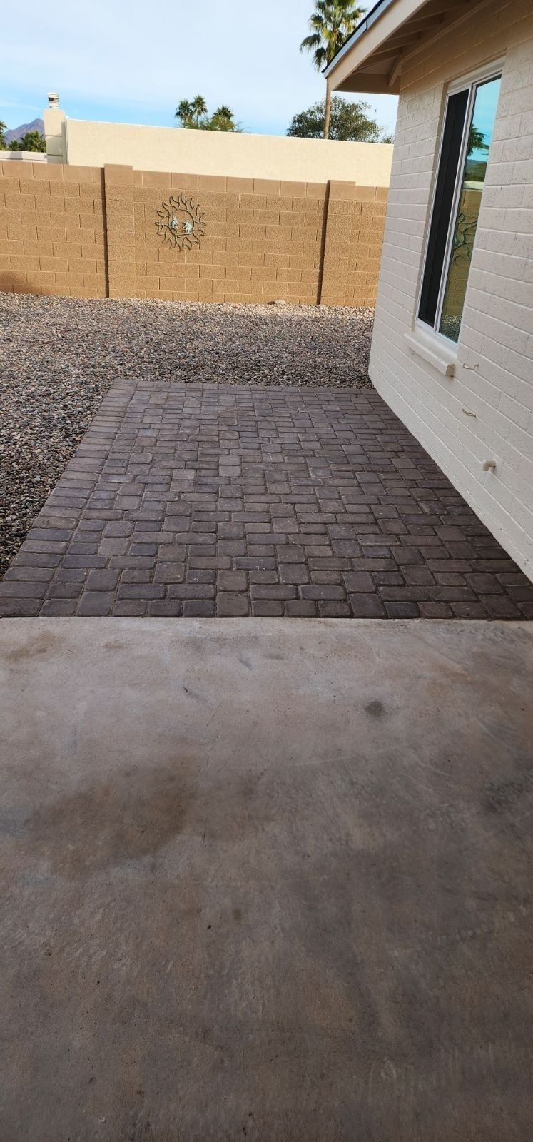 A brick walkway leading to a house with a fence in the background.