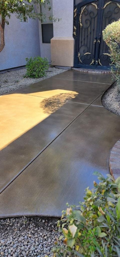 A concrete walkway leading to a house with a gate in the background.