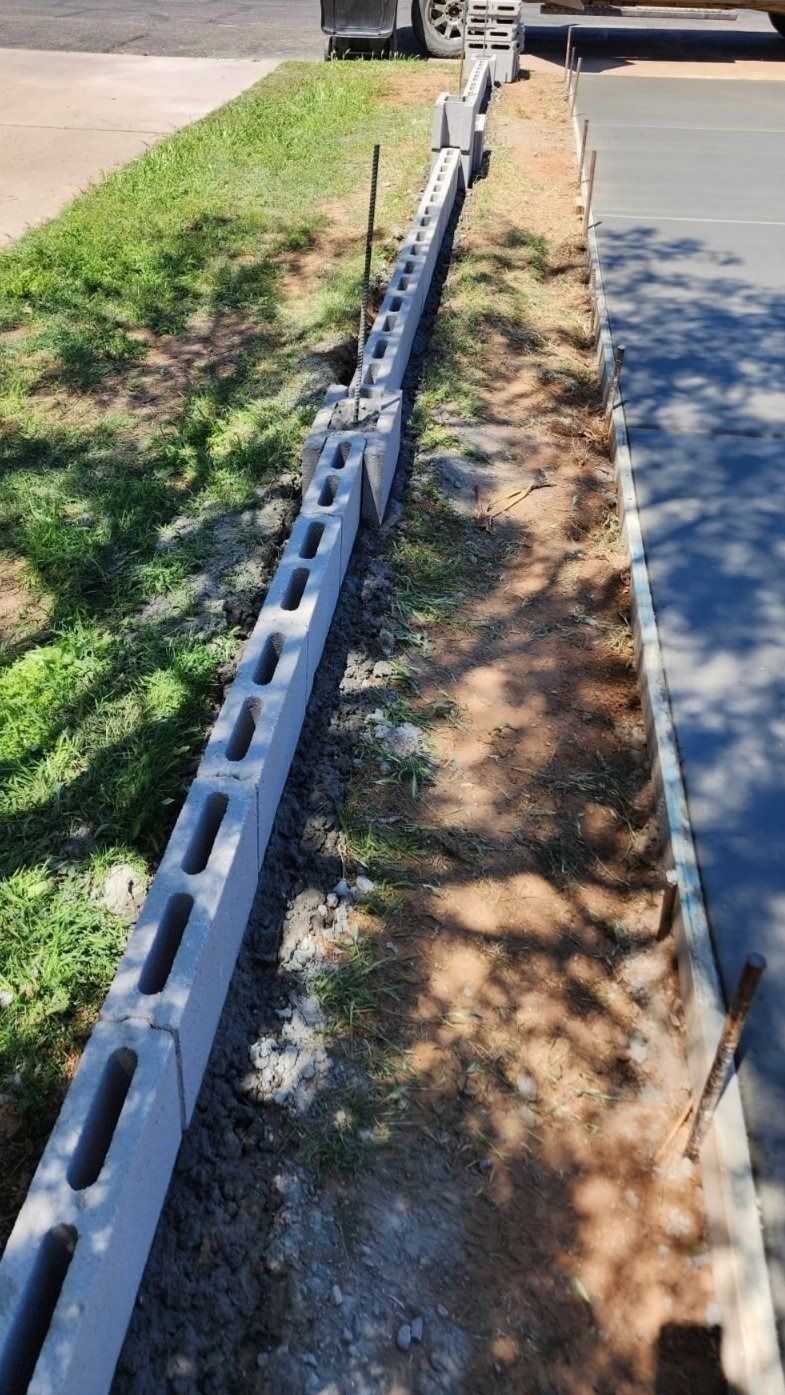 A concrete block fence is being built next to a driveway.