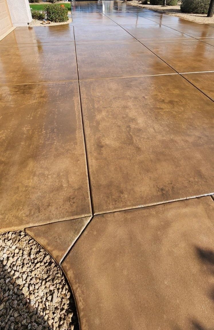 A close up of a concrete driveway with a sprinkler in the background.