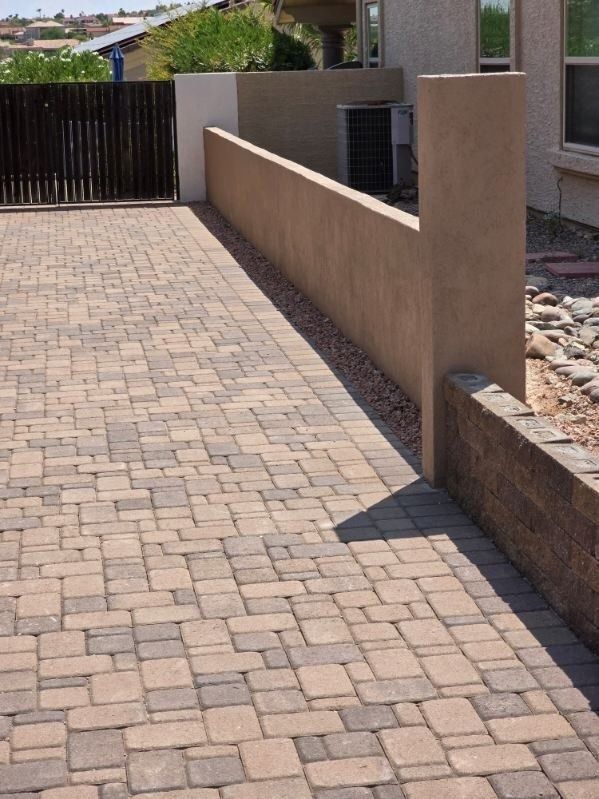 A brick driveway leading to a house with a fence