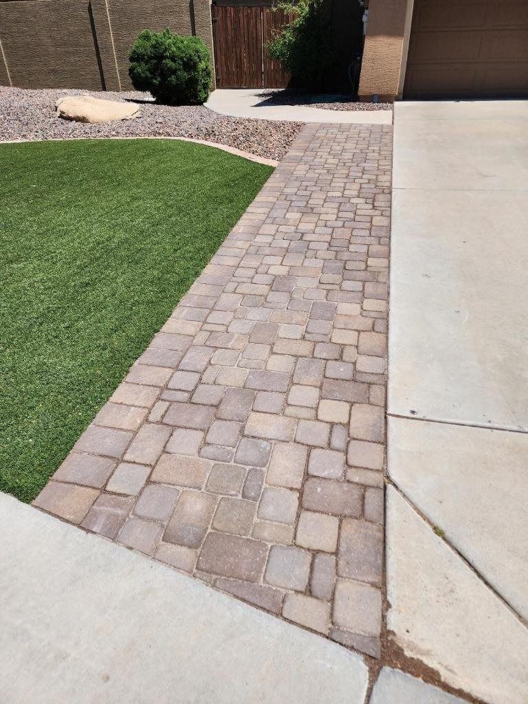 A brick walkway leading to a grassy yard next to a garage.