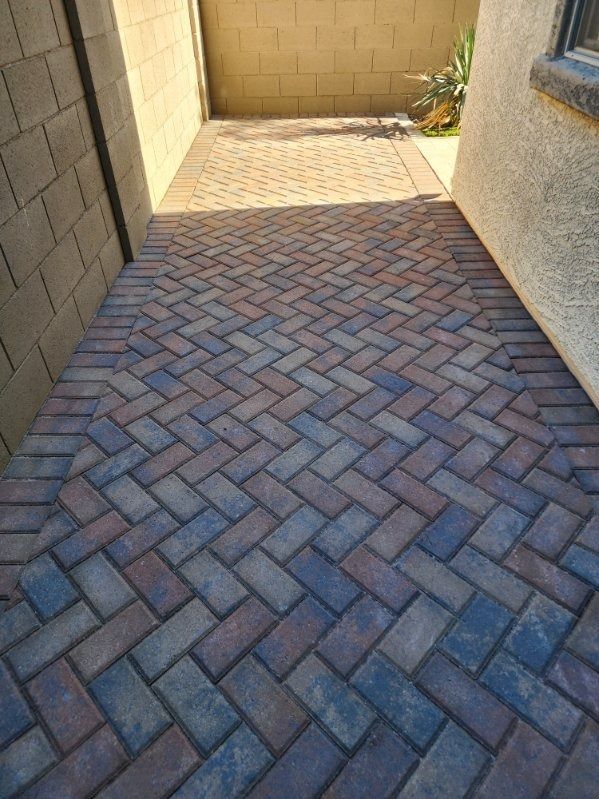 A brick walkway leading to a house with a herringbone pattern.