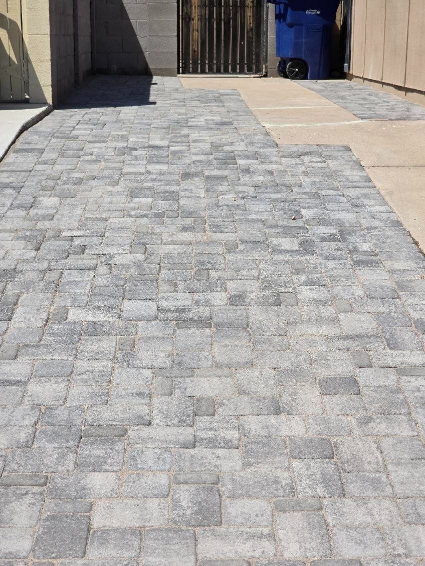 A brick walkway with a blue trash can in the background