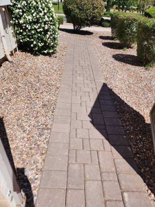 A brick walkway leading to a house with bushes on both sides.