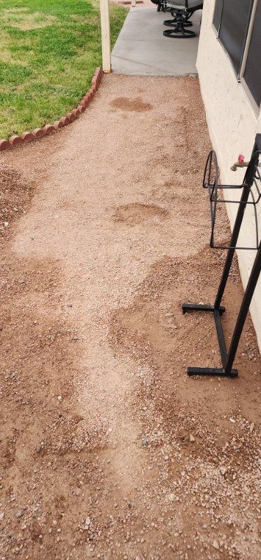 A dirt path leading to a patio next to a house.