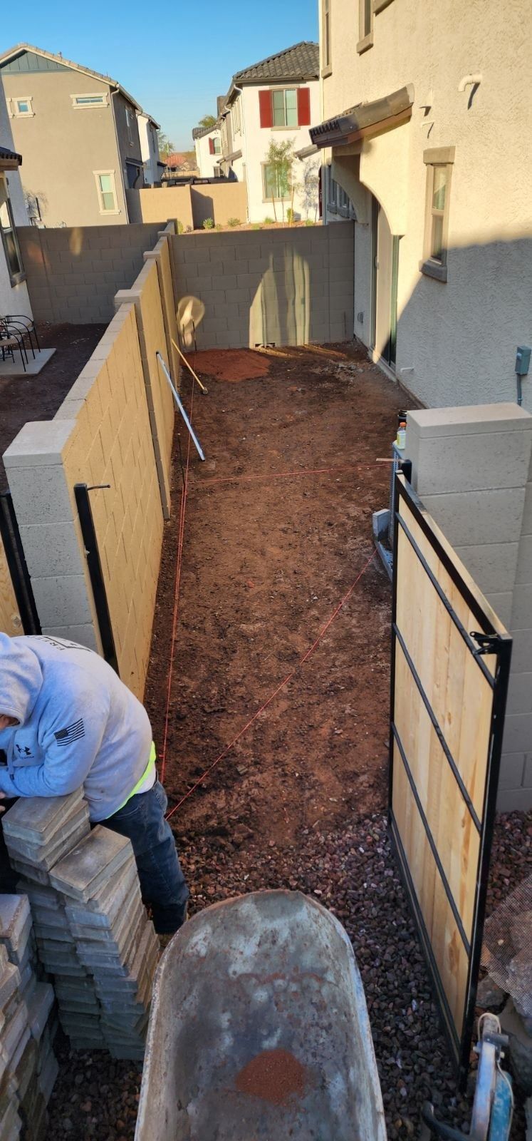 A man is working on a sidewalk next to a fence.