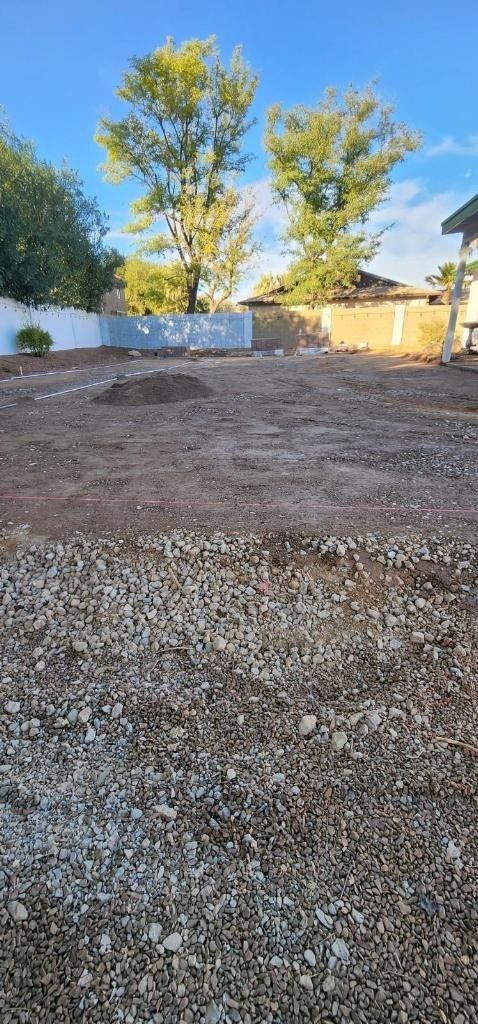A gravel lot with trees in the background and a house in the background.