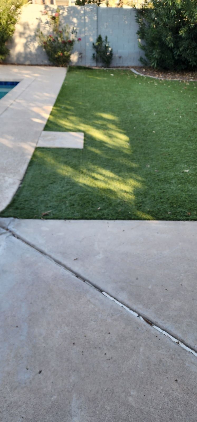 A lawn with a concrete walkway and a pool in the background.
