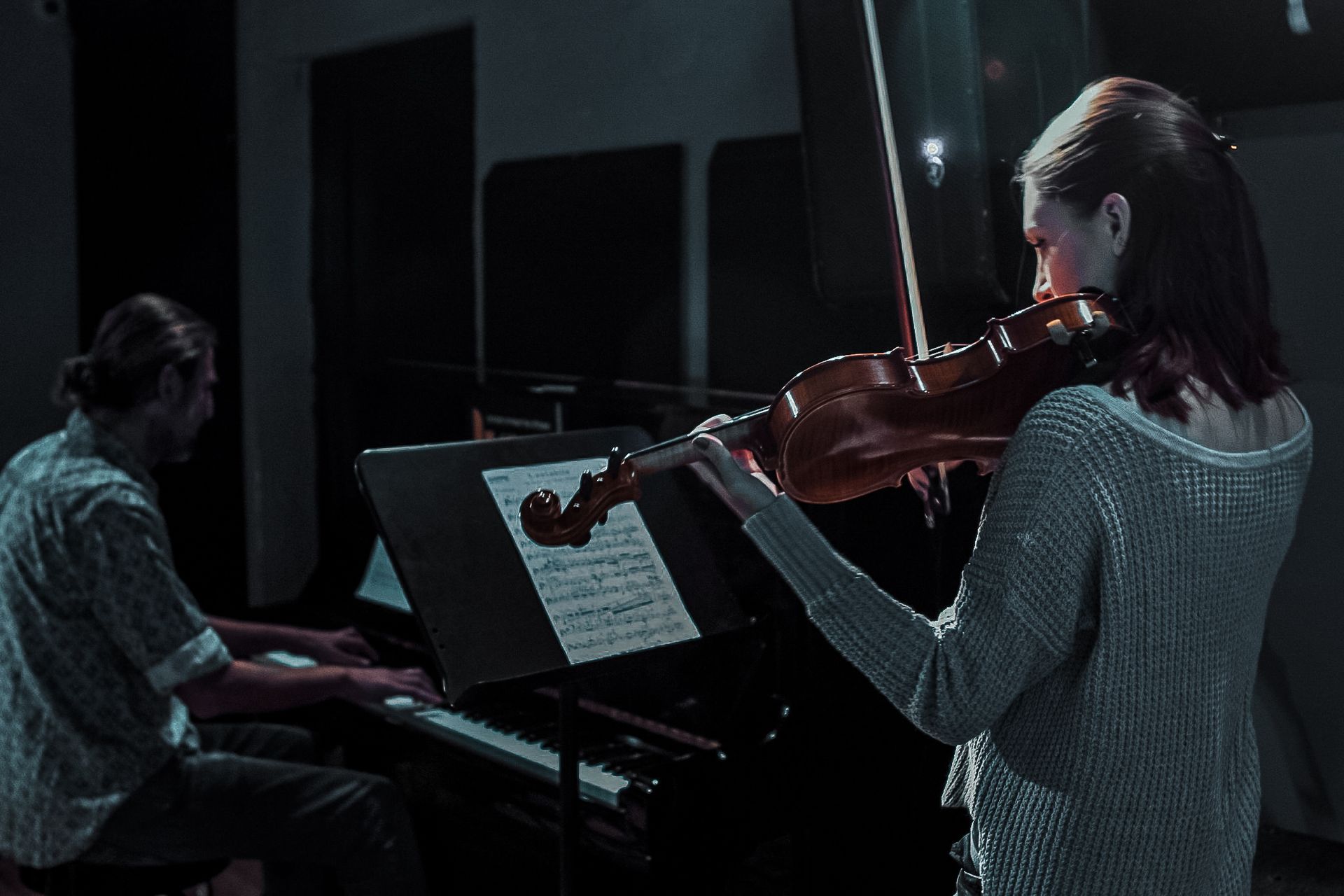 A man is playing a piano and a woman is playing a violin.