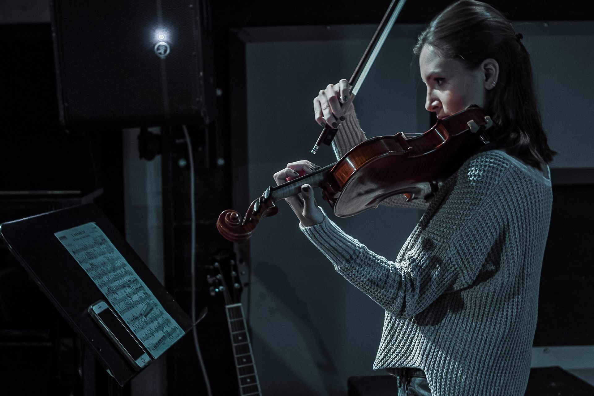 A woman is playing a violin in a dark room.