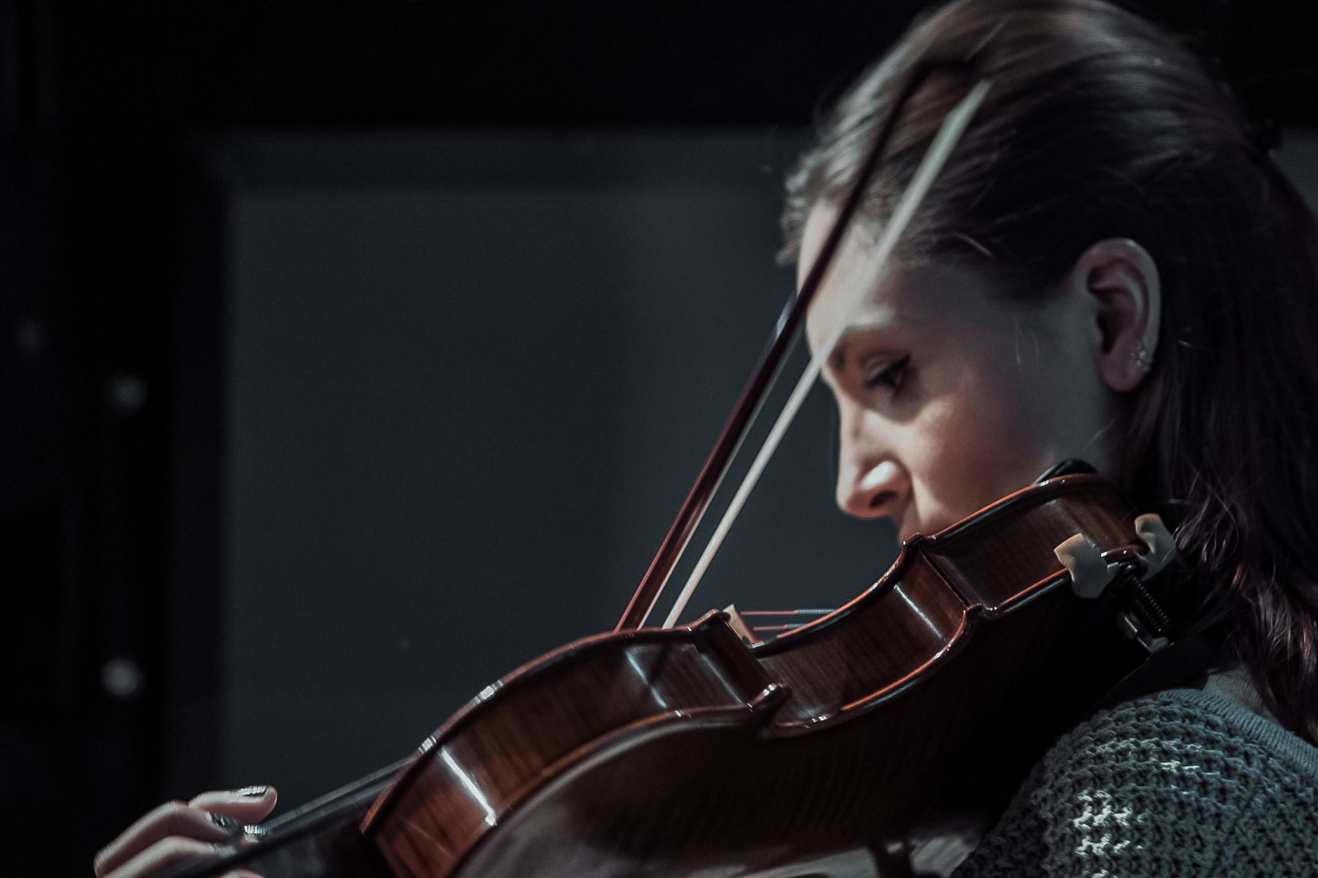 A woman is playing a violin in a dark room.