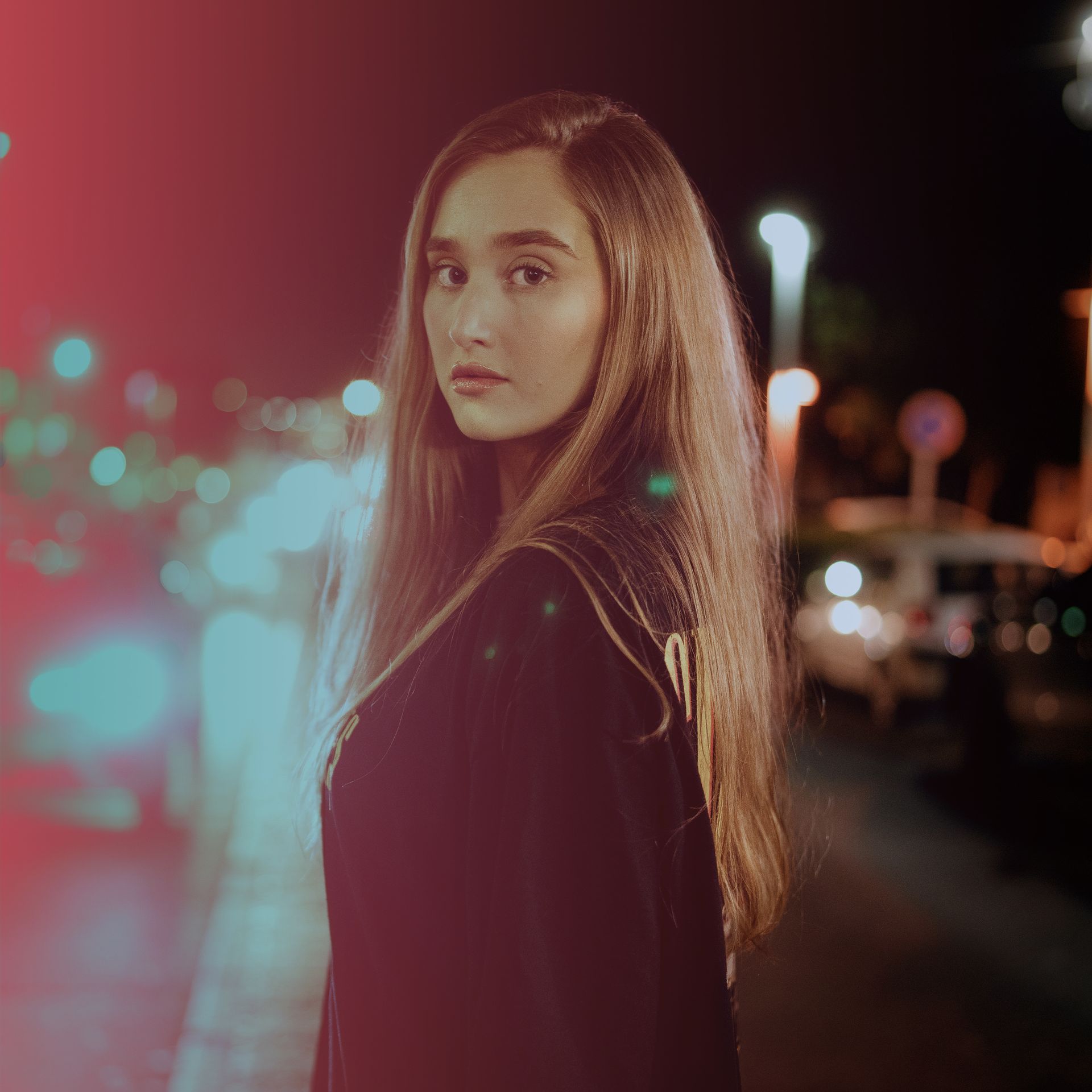 A woman with long hair is standing in a dark street at night.