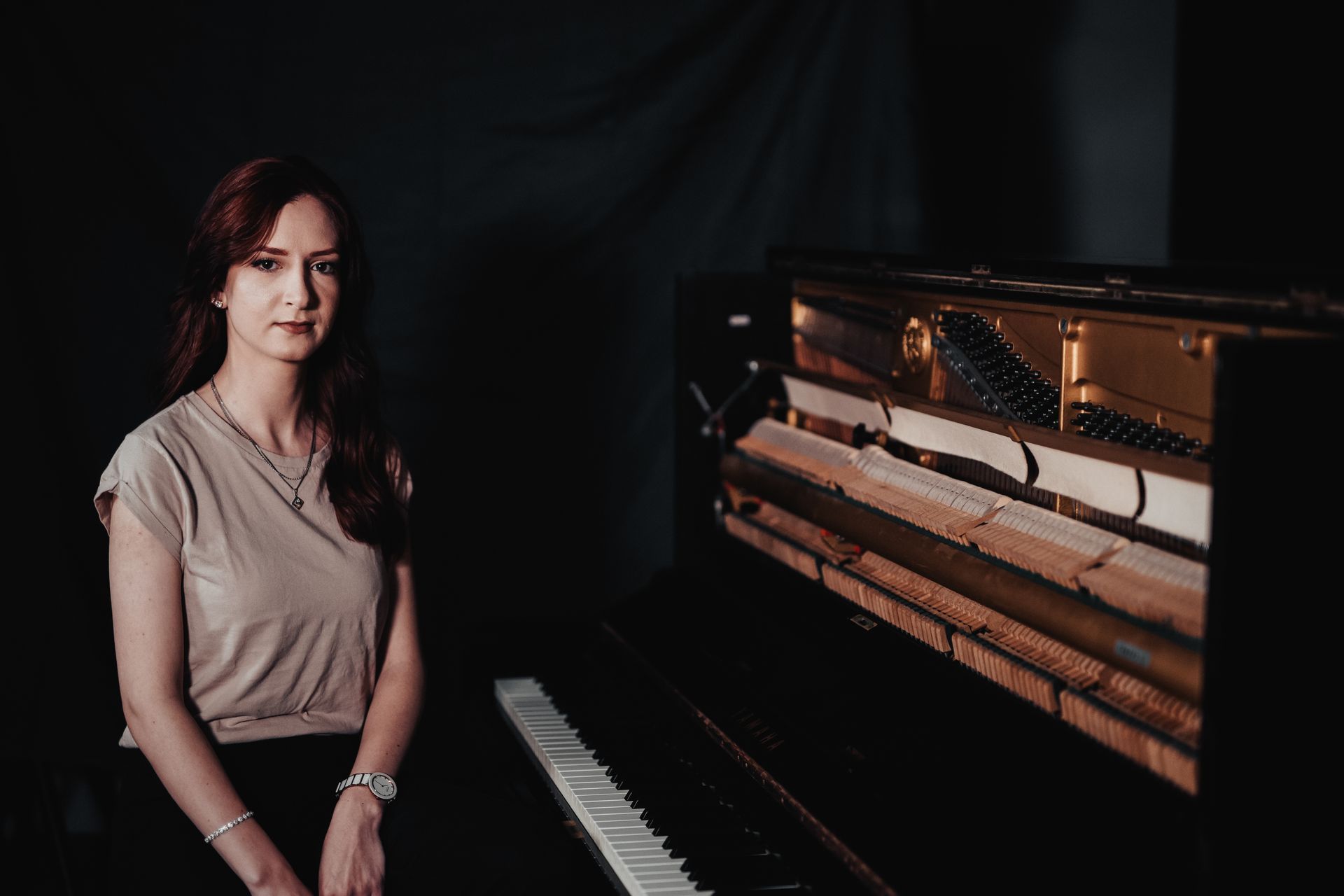 A woman is sitting in front of a piano in a dark room.