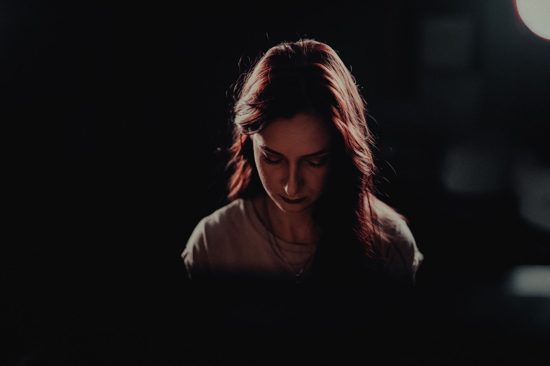 A woman is sitting in the dark looking down at something.