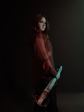 A woman in a red shirt is holding a guitar in a dark room.