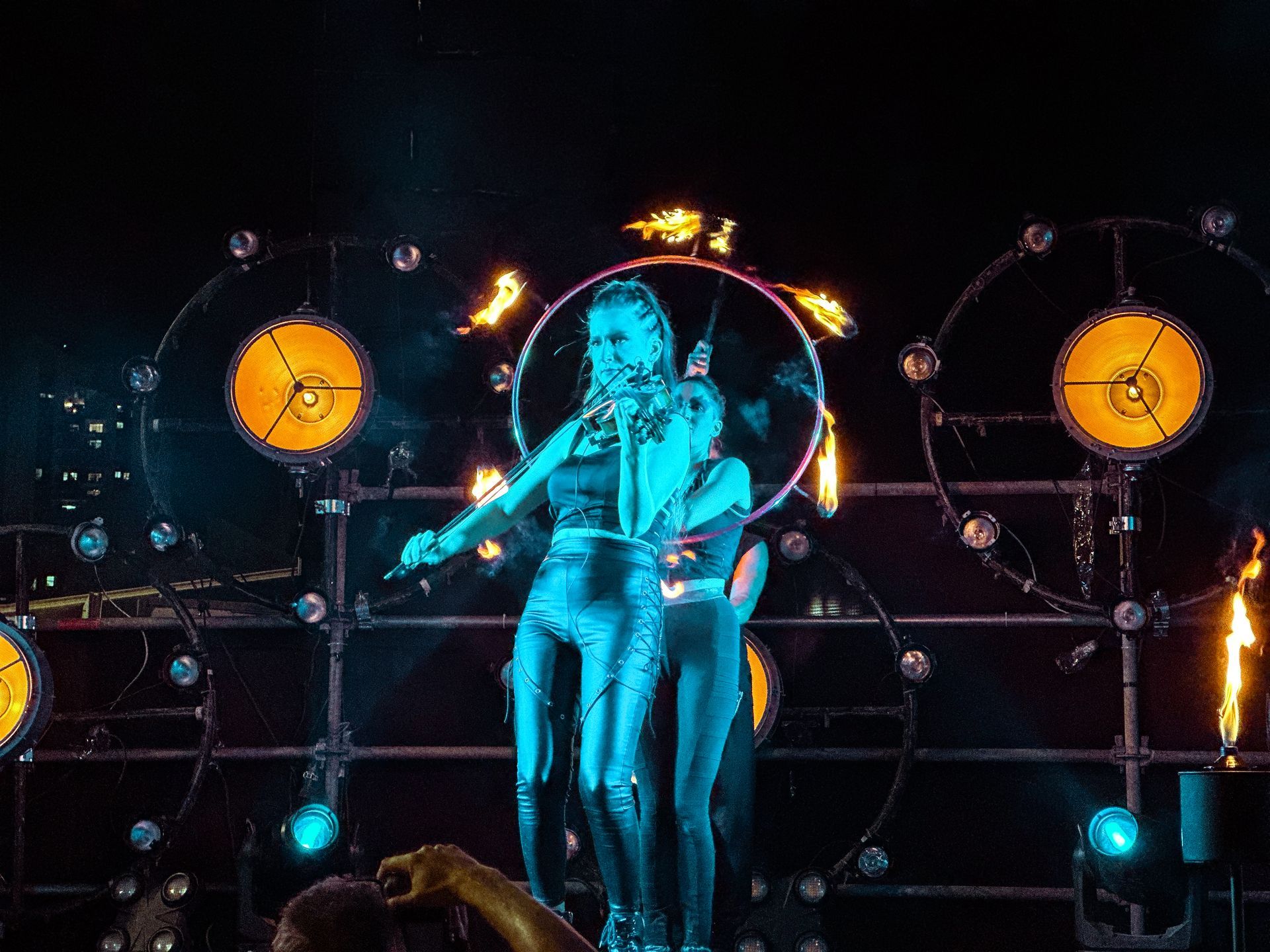 A woman is singing into a microphone on a stage surrounded by fire.