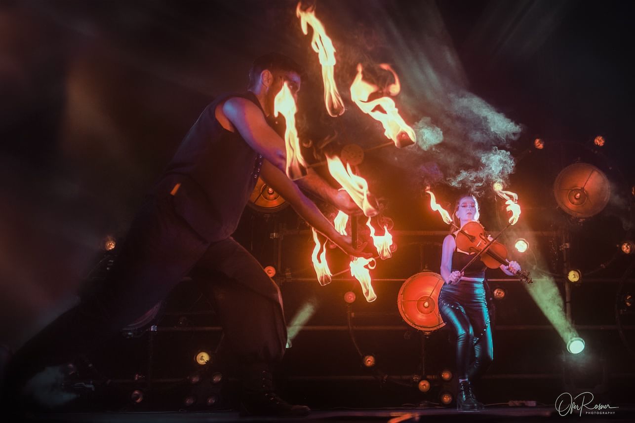 A woman is playing a violin on a stage with fire coming out of her hands.