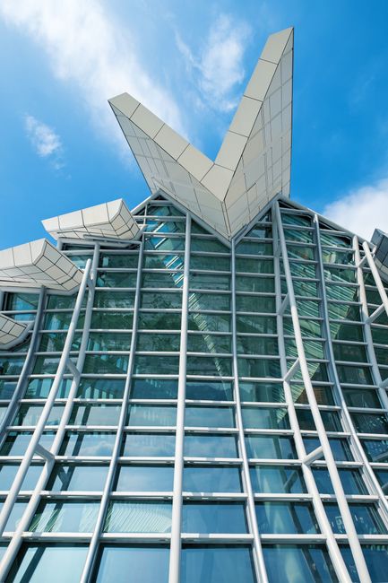 Modern building with glass and white geometric roof against a blue sky.