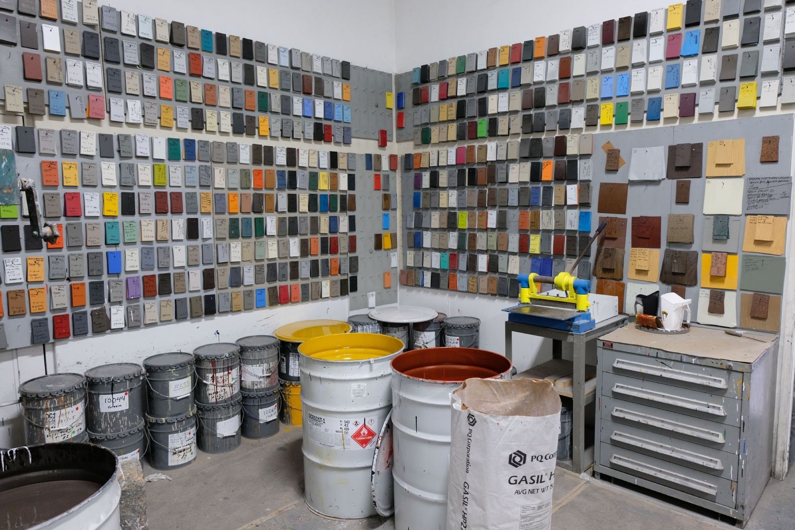 Room filled with colorful paint swatches on walls. Paint buckets and work table in foreground.