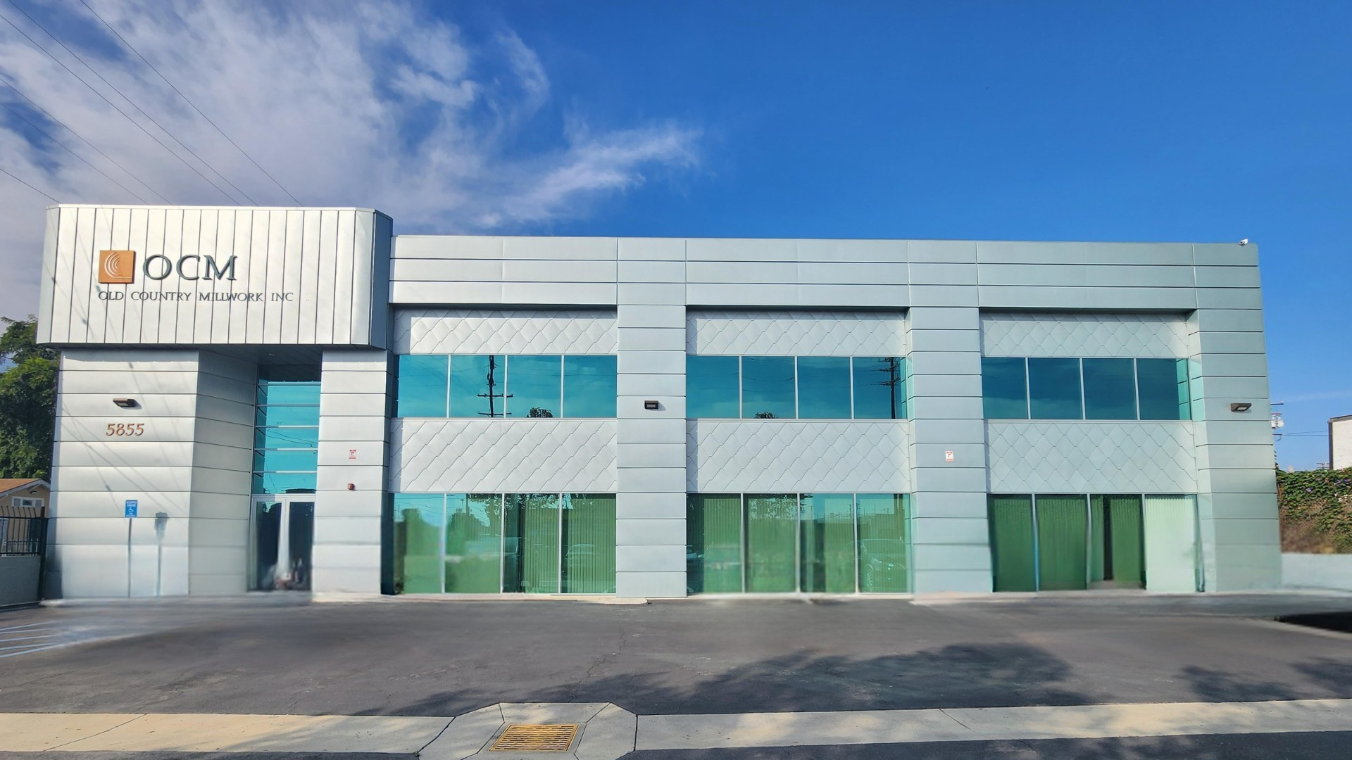 Gray building with orange logo, small bush, and metal fence on a sunny day.