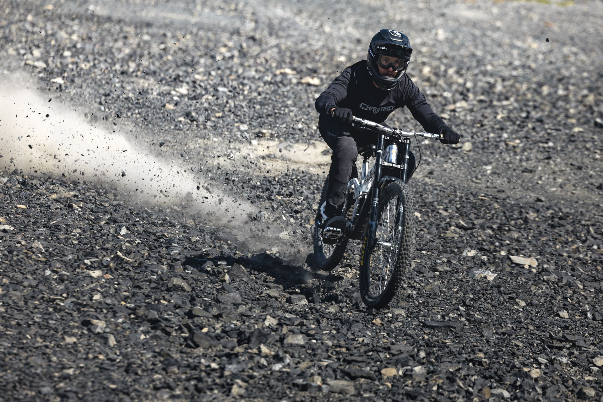 Mountain biker on a black bike, kicking up dust on a rocky, gray terrain.
