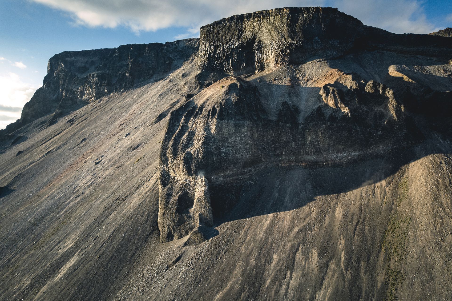 Gray, rocky mountain side under a blue sky. The mountain has a flat top and a long, sloping face.